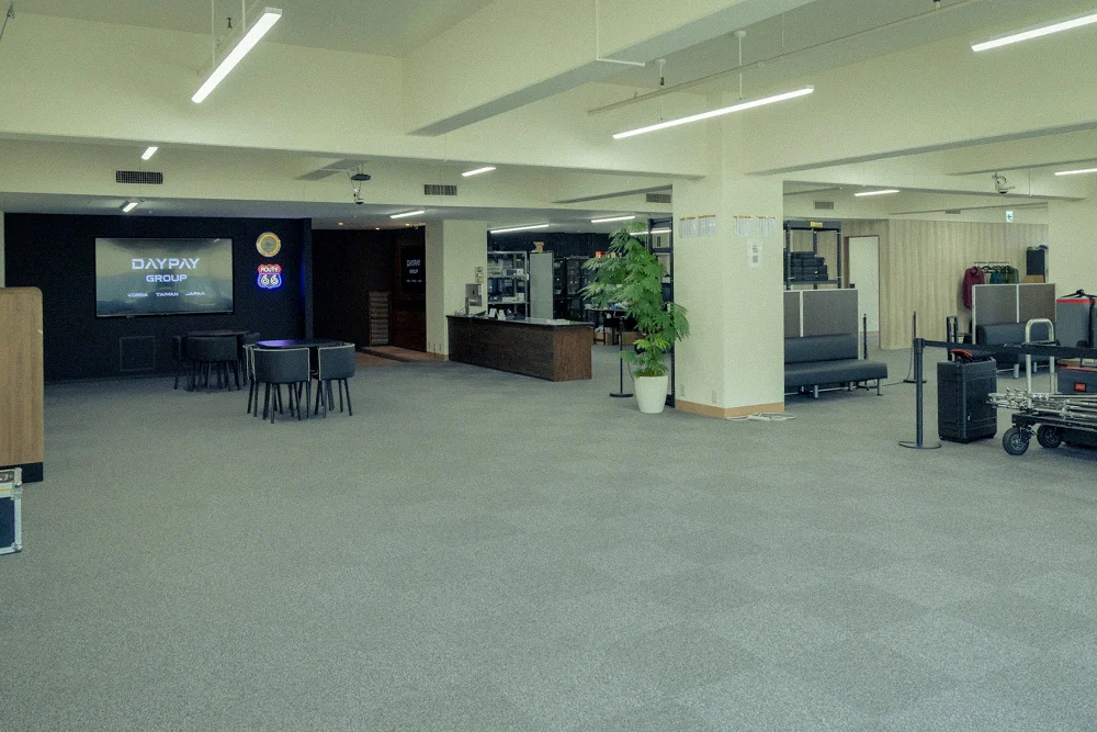 デイペイレンタル(DAYPAY RENTAL)の広々としたオフィス内の様子。デスクやテーブル、ディスプレイモニター、観葉植物が配置されています。