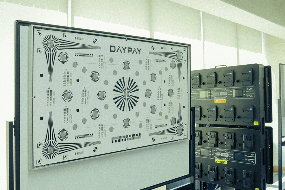 デイペイレンタル(DAYPAY RENTAL)のオフィス内に設置されたDAYPAYロゴ入りの大型フォーカスチャートと、バッテリーチャージャーが並ぶ設備スペース。