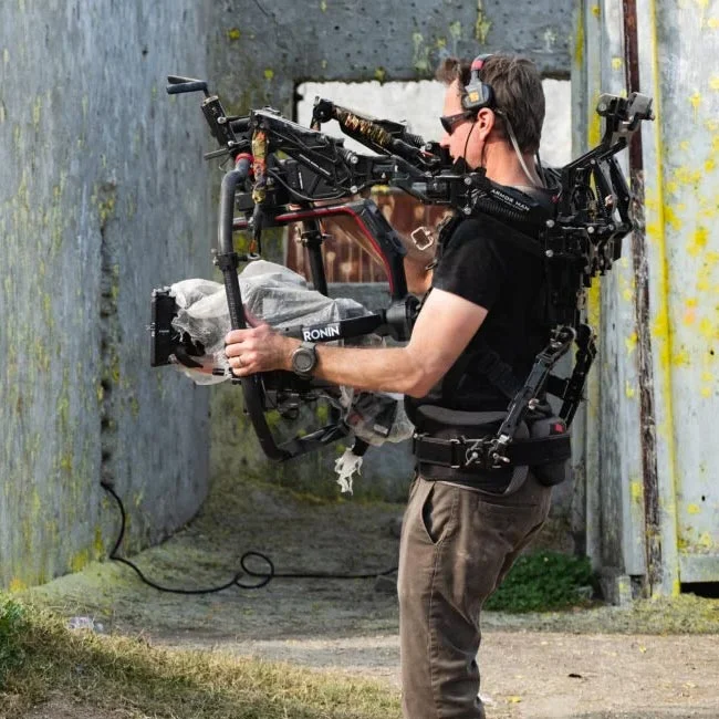 Tilta Armorman 3.0 支撐系統操作者側身實拍，展示穿戴背心與雙機械減震臂連接穩定器狀態